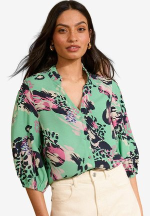Blusa verde de botones con patrones florales en negro, rosa y azul. Presenta mangas cortas abullonadas y un cuello, hecha de tejido ligero.