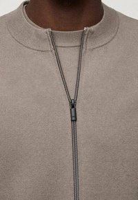 Light brown zip-up sweater with a high collar, featuring a matte metal zipper and smooth knit texture. No patterns or graphics visible.