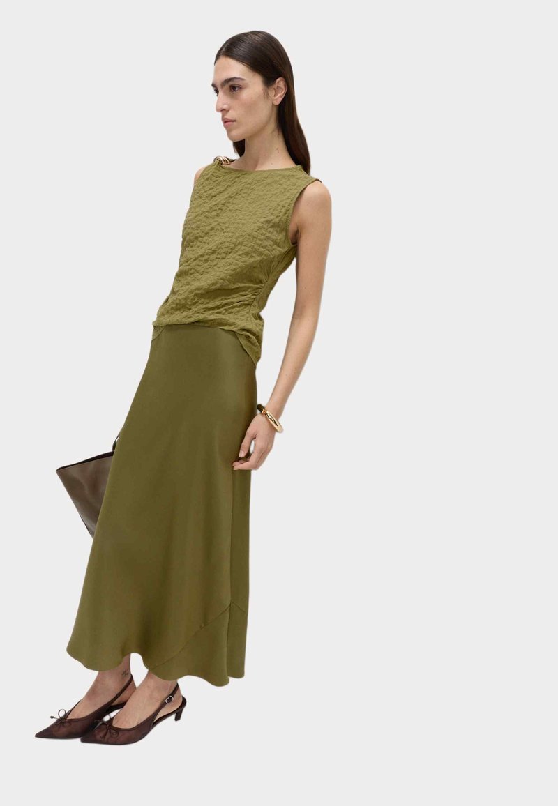 Olivgrön texturerad ärmlös topp med rundad halsringning, tillsammans med en matchande flödande kjol. Bruna slingback-klackar och en mörk handväska.