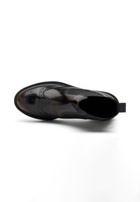 Zapato tipo mocasín en cuero negro y marrón con diseño de brogue, paneles elásticos en los laterales y suela de goma texturizada.
