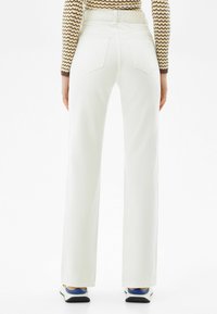 White flared jeans with a high waist, two back pockets, and a smooth texture, paired with blue and white sneakers.