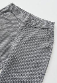 Black and white patterned pants with a textured fabric, elastic waistband, and side pockets. Features a geometric design throughout.