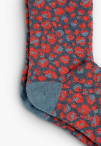 Calcetín azul con estampado de leopardo rojo, que presenta una textura suave y un puño acanalado. La puntera y el talón tienen un acento azul sólido.