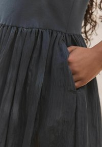 Donkerblauwe jurk met een slim-fit lijfje en een uitlopende, textuurrijke rok. Beschikt over een gegatherde tailleband en een zijzak, met een subtiele glans.
