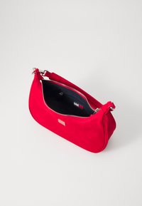 Sac à main synthétique rouge avec une texture lisse, une forme incurvée et une fermeture éclair argentée. L'intérieur est d'un bleu sombre avec une petite étiquette visible.