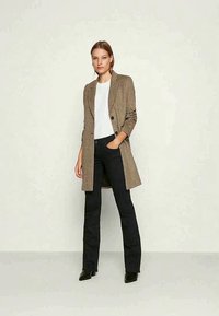 Brown checked blazer with a tailored fit, long sleeves, single button closure; paired with a white top and black flared jeans.