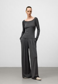 Grå långärmad topp med vid halsringning, matchad med löst sittande, plisserade grå byxor. Slätt tyg med en mjuk textur och neutrala detaljer.