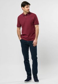 Bordó polo tričko s krátkým rukávem a límečkem, spojené s tmavě modrými skinny džíny a námořnickými teniskami.