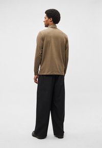 Pruun pikkade varrukatega särk kõrge kraega, sobitatud mustade laiade sääristega pükstega. Sile kangapind koos külgsete lõhikuga ääres.