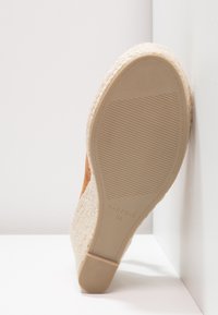 Semelle d'une chaussure compensée espadrille beige avec une semelle en caoutchouc texturée, de la marque "PARFOIS" et de taille 36, affichée contre un mur blanc.