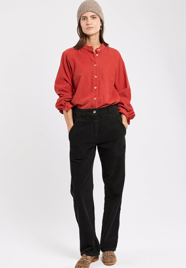 Chemise rouge à boutons avec un col et des manches froncées, associée à un pantalon en velours côtelé noir avec des poches latérales. Chaussures à enfiler à imprimé animal.
