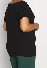 Svart kortärmad topp med avslappnad passform, rund halsringning och mjuk tygtextur. Kombinerad med gröna byxor.