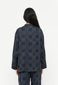 Camisetta navy con stampa geometrica caratterizzata da forme contornate, maniche lunghe e taglio dritto, realizzata in un tessuto leggero e liscio.
