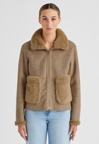 Braune Kunstfelljacke mit Reißverschluss, großen frontalen Taschen und einem weichen, zotteligen Kragen. Verfügt über eine kuschelige Textur und eine taillierte Passform.