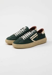 Sneaker verde scuro con tessuto texturizzato, lacci bianchi e accenti crema. Presenta una suola intrecciata color cuoio e un marchio sulla linguetta.