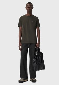 Oliivivihreä t-paita pyöreällä pääntiellä, yhdistettynä leveälahkeisiin mustiin farkkuihin ja tikkikuoriseen mustaan laukkuun. Teksturoituja tennareita käytetään asusteena.