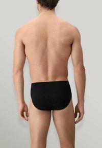 Slip da bagno neri, realizzati in tessuto morbido, caratterizzati da un design a vita bassa e bordi senza cuciture per il massimo comfort. Vista posteriore che mostra una copertura minima.