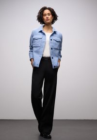 Jasnoniebieska koszula z mieszanki wełny z dwoma kieszeniami na piersi, czarnymi guzikami i prostym krojem, zestawiona z czarnymi spodniami z wysokim stanem.