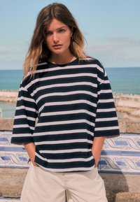 Navy and white striped short-sleeve t-shirt with a relaxed fit, round neckline, and subtle texture. Paired with light beige shorts.