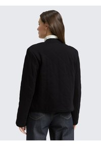 Zwarte gewatteerde jas met een hoge hals, gemaakt van gladde stof en met lange mouwen. De achterkant is eenvoudig, zonder zichtbare sluitingen of accenten.