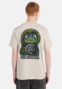 Μπεζ βαμβακερό κοντομάνικο με πολύχρωμη απεικόνιση βατράχου με ακτίνες ήλιου και κείμενο "ELEMENT TIMBER SEEKERS" στην πλάτη.