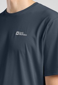 T-shirt bleu foncé à manches courtes avec une texture lisse et légère et un petit logo blanc sur la partie gauche de la poitrine.