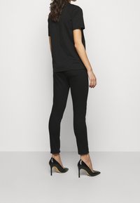 Svart bomullströja och svarta åtsittande byxor, ihop med spetsiga svarta högklackade skor. Tyget ser slätt ut, med en enkel design och inga synliga mönster.