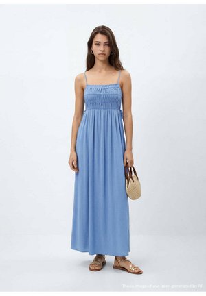 Frau trägt ein langes hellblaues ärmelloses Kleid mit Spaghettiträgern, hält eine kleine geflochtene Handtasche und trägt goldene Sandalen.