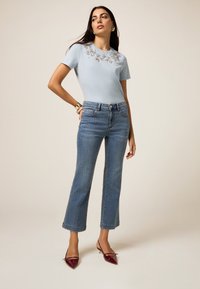 Camiseta de algodón azul claro con bordado floral en el escote, combinada con jeans de pierna recta de talle alto y tacones de charol burdeos.