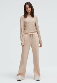 Beiges, geripptes Lounge-Set mit langen Ärmeln, Kordelzug in der Taille und weit geschnittenen Hosenbeinen. Weiche Textur mit entspannter Passform.