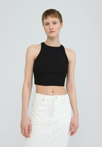 Black ribbed crop top with a high neckline, paired with a white denim skirt featuring a front slit and button closure.