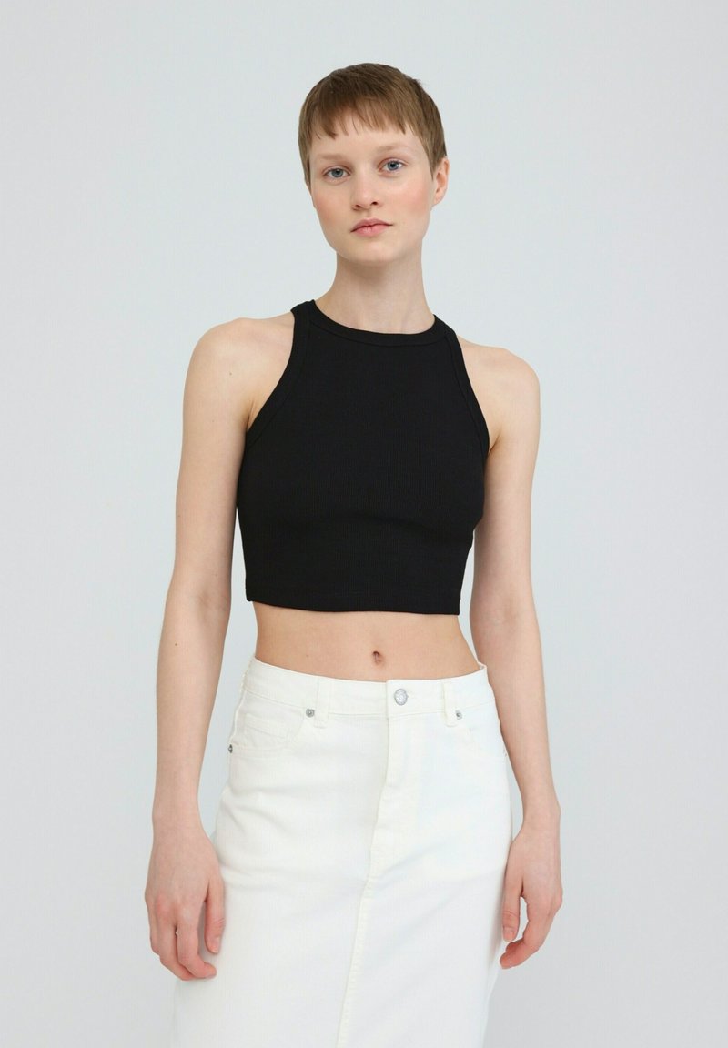 Black ribbed crop top with a high neckline, paired with a white denim skirt featuring a front slit and button closure.