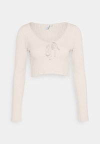 Haut crop top manches longues beige clair en tissu côtelé, avec un col en V et un détail noué à l'avant pour un ajustement réglable.