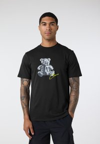 Black T-shirt featuring a glossy, silver teddy bear graphic centered on the front, accented by yellow text below the bear. Short sleeves.
