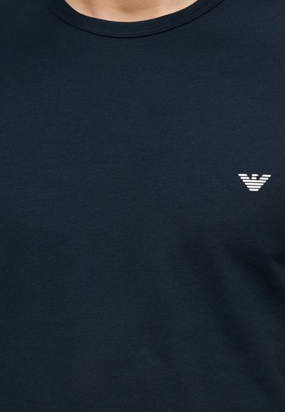 Σκούρο μπλε κοντομάνικο μπλουζάκι με στρογγυλή λαιμόκοψη και μικρό λευκό στυλιζαρισμένο λογότυπο πουλιού στο αριστερό μέρος του στήθους.