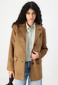 Brown suede blazer with a notched collar, single button closure, and two front pockets, paired with a light green button-up shirt.