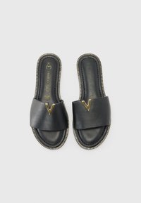 Sandales en cuir noir avec de larges straps croisées, ornées d'un détail en V doré, contrastées par une bordure en tan cousue sur la semelle. Taille 37.