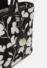 Dekorativní kabelka s květinovým vzorem v černobílé kombinaci, s texturovaným povrchem, z kulatým kovovým logem a zipovým uzávěrem.