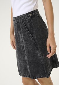 Fustă din denim de culoare gri închis cu un finisaj ușor decolorat. Prezintă talie înaltă, pliuri în față, buzunare laterale și un singur sistem de închidere cu buton metalic.