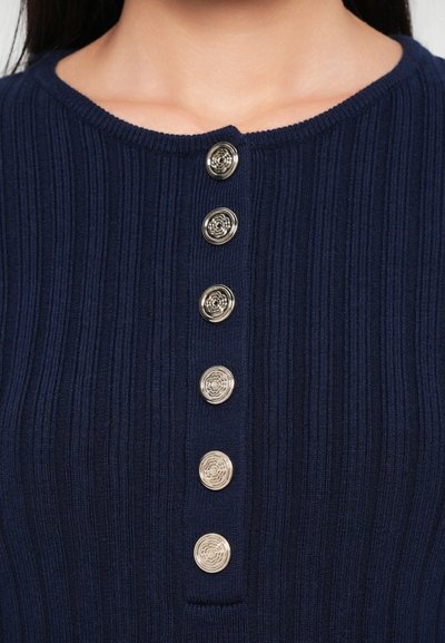Marine ribbestrikket topp med rund hals og seks metalliske blomsterknapper foran. Glatt tekstur med en tettsittende silhuett.