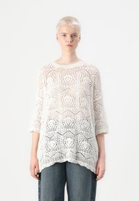 Pull blanc en tricot ouvert avec un motif géométrique, col rond et manches trois-quarts. Tissu léger et finition texturée.