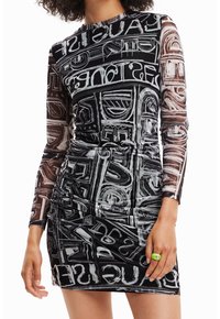 Robe moulante noire avec manches longues en tulle transparent ornées d'un motif graphique blanc. Le tissu a une texture lisse et légèrement brillante avec des détails froncés.