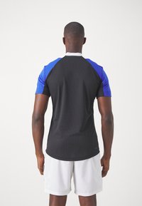 Korte mouwen sportshirt met een zwart lichaam, blauwe raglanmouwen en een witte kraag, gemaakt van vochtafvoerende stof.