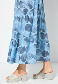 Pitkä sininen mekko, jossa on pyöreä kuvio sinisen ja harmaan sävyissä. Yhdistetty vaaleanharmaisiin paksupohjaisiin sandaaleihin.