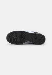 Suola nera di una sneaker Nike con motivi a trama circolare e a griglia su uno sfondo bianco.