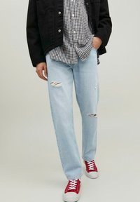 Jeans chiari, strappati e usurati; abbinati a una giacca nera e a una camicia a scacchi bianca e nera. Sneakers rosse completano il look.