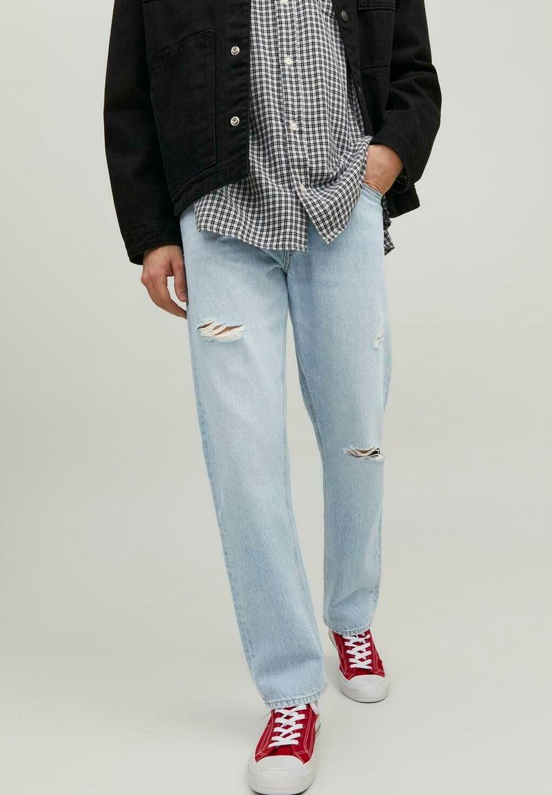 Jeans chiari, strappati e usurati; abbinati a una giacca nera e a una camicia a scacchi bianca e nera. Sneakers rosse completano il look.