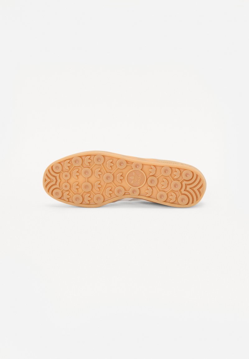 Suela de zapato de goma, con un patrón texturizado que presenta agarraderas circulares y un logo en el centro. El color es marrón claro con un acabado suave.