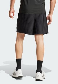 Shorts de sport noirs texturés avec des rayures verticales et une taille élastique. Portés avec des chaussettes noires et des baskets blanches.