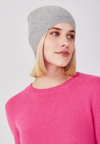 Un bonnet en tricot ribbé gris sur une personne ayant les cheveux blonds, associé à un pull rose vif avec un col rond.